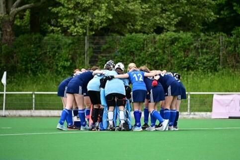 Mannschaft von Hockeyspielerinnen bildet einen Kreis auf dem Spielfeld zum gemeinsamen Anfeuern vor dem Spiel.