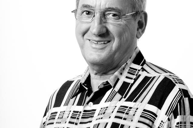 Portr&auml;t eines l&auml;chelnden Mannes mit Brille in einem karierten Hemd vor einem wei&szlig;en Hintergrund.