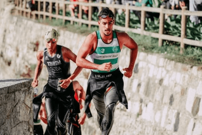 Zwei m&auml;nnliche Triathleten laufen nebeneinander auf einem gepflasterten Weg w&auml;hrend eines Wettkampfs.