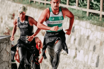 Zwei männliche Triathleten laufen nebeneinander auf einem gepflasterten Weg während eines Wettkampfs.