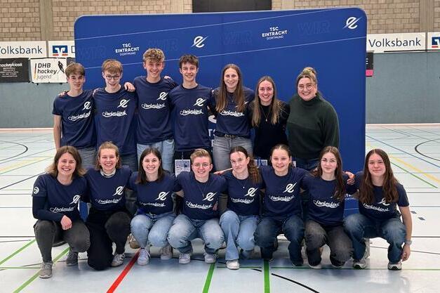 Gruppe junger Menschen in blauen T-Shirts posiert l&auml;chelnd vor einer Wand mit dem Logo des TSC Eintracht.