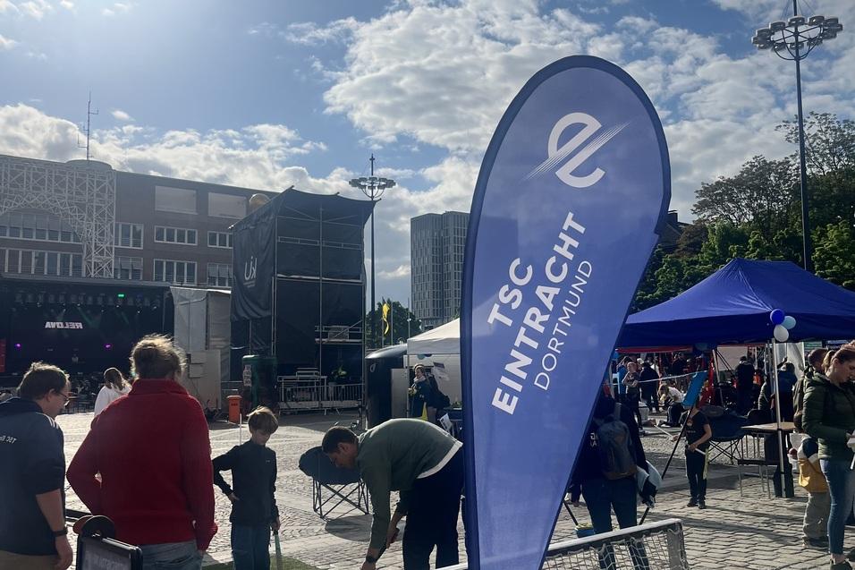 Zelt mit TSC Eintracht Dortmund-Logo, Sportaktivit&auml;ten und Menschen auf einem Platz bei sonnigem Wetter.