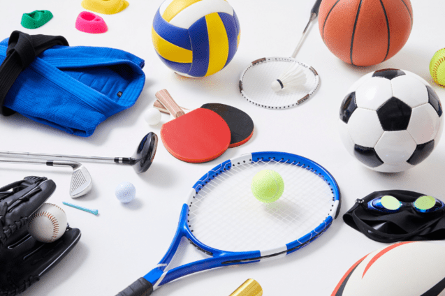 Vielfalt an Sportger&auml;ten: Tennis- und Basketball, Fu&szlig;ball, Golf, Tischtennis, Schwimmbrille und weitere bunte B&auml;lle auf Tisch.