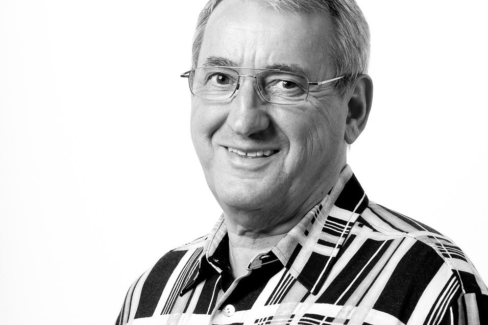 Portr&auml;t eines l&auml;chelnden Mannes mit Brille in einem karierten Hemd vor einem wei&szlig;en Hintergrund.