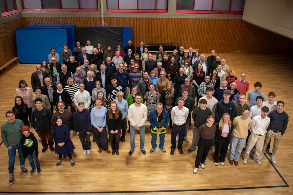 Gruppeneinheit von &uuml;ber 100 Personen in einem Sportraum, verteilt auf einer Holzfl&auml;che, einige halten B&auml;lle.