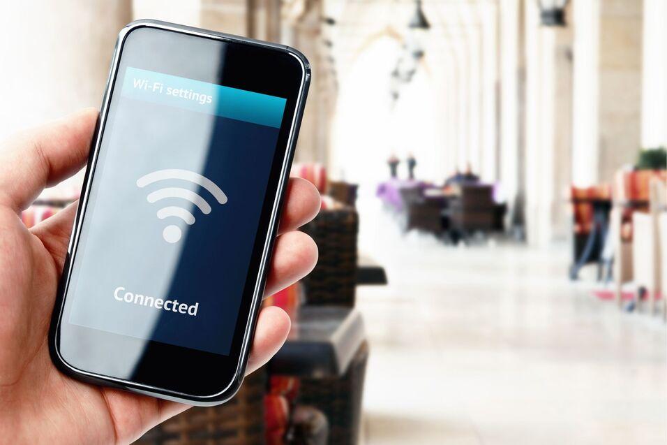 Hand hält Smartphone mit Anzeige „Connected“ und WLAN-Symbol in einem modernen, hellen Innenraum.