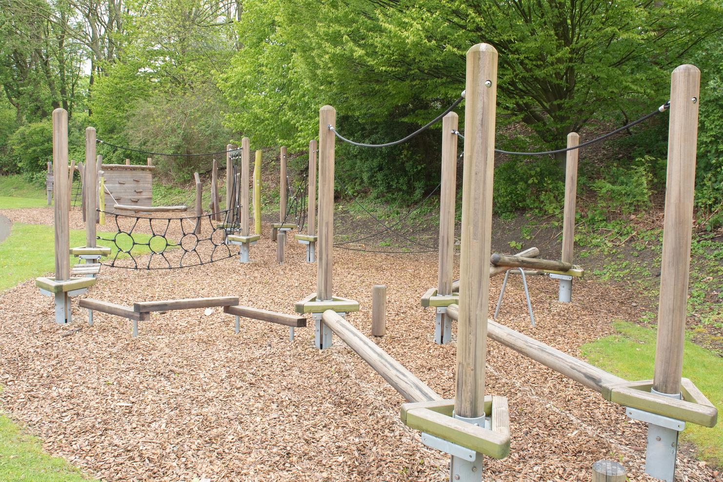 Holzspielger&auml;t mit Kletterelementen und Seilen auf einer Spielplatzfl&auml;che mit Holzhackschnitzeln im Gr&uuml;nen.