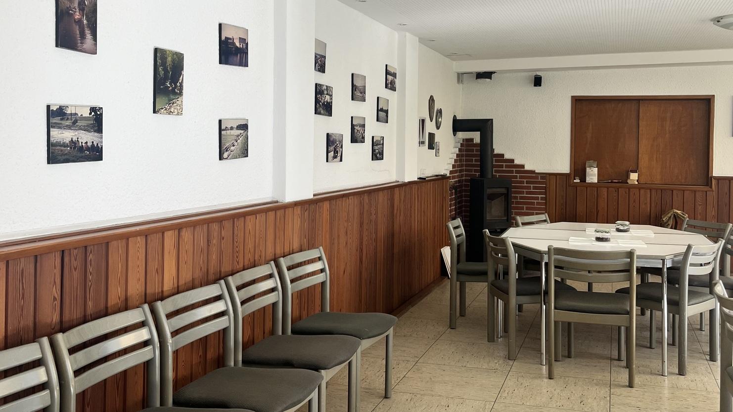 Innenansicht eines Raumes mit einem runden Tisch, St&uuml;hlen und Bildern an der Wand. Holzvert&auml;felung und helles Deckenlicht.