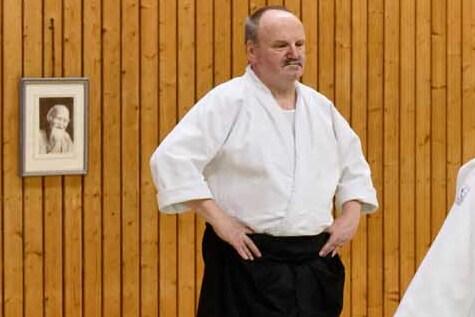 Zwei Aikidokas f&uuml;hren eine Technikausf&uuml;hrung mit &Uuml;bungsstangen auf einer Tatami in einem Dojo durch.