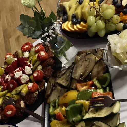 Buffet mit Spie&szlig;en, gef&uuml;llten Paprikas und frischem Obst, umgeben von einem kleinen Blumenarrangement.