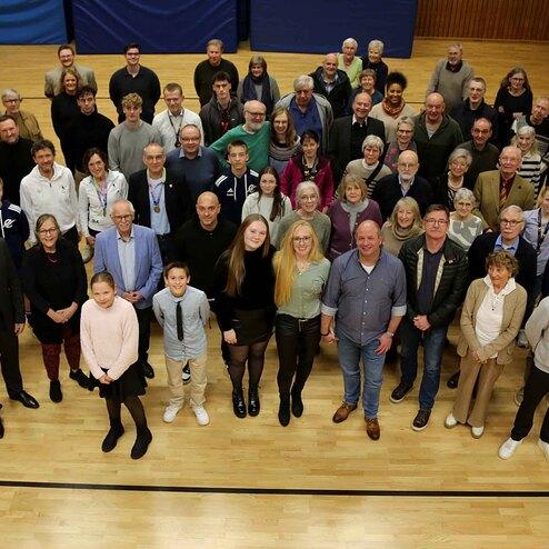Gruppenfoto von &uuml;ber 50 Personen in einem gro&szlig;en Raum, alle stehen auf einem Holzboden, l&auml;cheln in die Kamera.