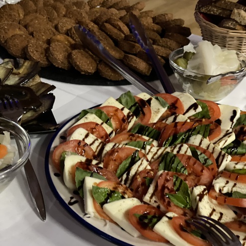 Bunte Platte mit Mozzarella, Tomaten und Basilikum, umgeben von verschiedenen Snacks und Brot.