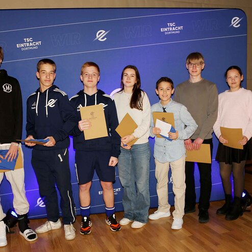 Gruppe von sieben Jugendlichen steht vor einer blauen Kulisse, jeder h&auml;lt eine Urkunde oder eine Auszeichnung in der Hand.