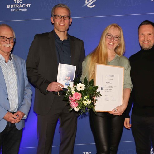 Gruppenszenen von vier Personen bei einer Ehrung, eine Person h&auml;lt eine Urkunde und einen Blumenstrau&szlig;.