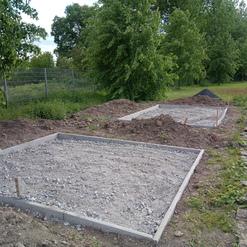 Baugrundst&uuml;cke mit Schotterunterlagen und Erdaufsch&uuml;ttungen, umgeben von B&auml;umen und Gras.