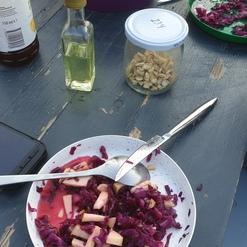 Teller mit Rotkohl und Apfelst&uuml;cken auf einem Holztisch, daneben ein &Ouml;l-Flasche, ein Glas mit N&uuml;ssen und eine gro&szlig;e Sch&uuml;ssel.