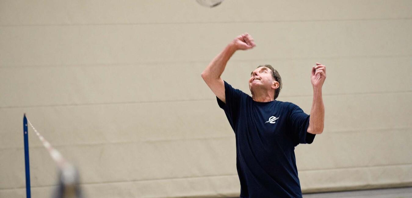 Ein Mann spielt Volleyball in einer Halle und bereitet sich auf einen Aufschlag.