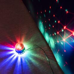 Drehende Farb-Lichtkugel projiziert bunte Muster auf eine Wand, daneben liegt der Lichtquelle ein dunkler Boden.