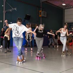Gruppe von Menschen auf Rollschuhen in einer Sporthalle, die synchron auf einer Fl&auml;che gleiten.