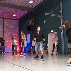 Gruppen von Menschen skaten auf Rollschuhen in einer beleuchteten Halle mit bunten Lichtern und reflektierendem Boden.