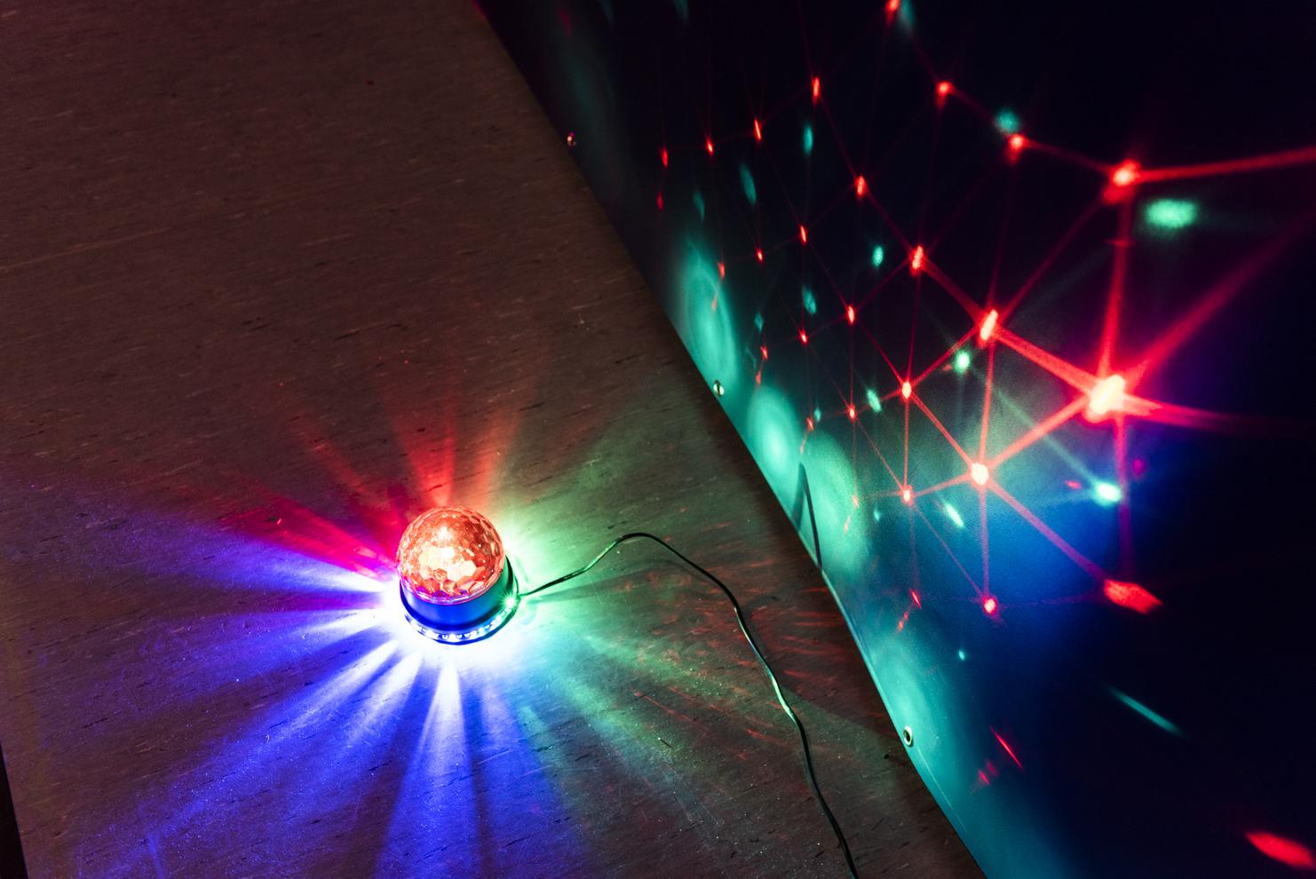 Drehende Farb-Lichtkugel projiziert bunte Muster auf eine Wand, daneben liegt der Lichtquelle ein dunkler Boden.
