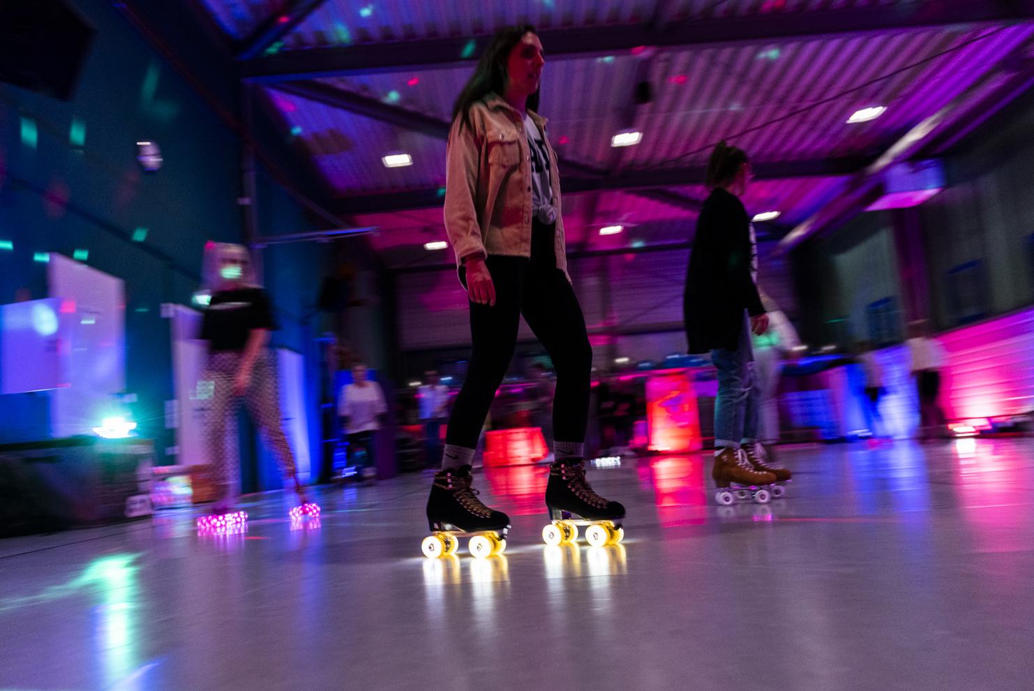 Person in Rollschuhen bewegt sich in einer beleuchteten Halle mit bunten Lichtern und reflektierenden Oberfl&auml;chen.