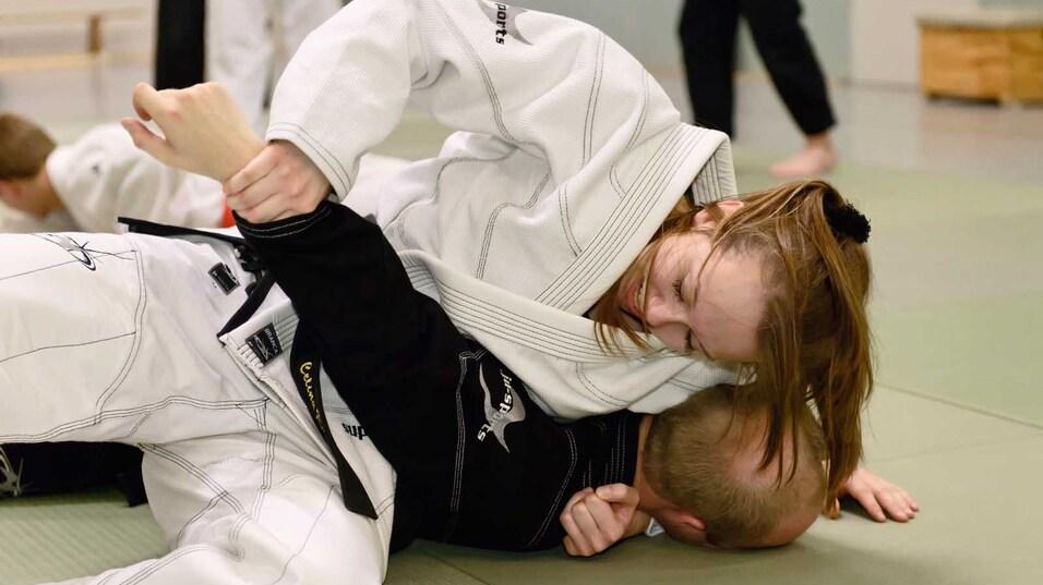 Nahaufnahme eines Zweikampfs im Judo, eine Person im wei&szlig;en Gi h&auml;lt einen Gegner im schwarzen Gi am Boden.
