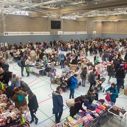 Vollbesetzte Halle mit zahlreichen St&auml;nden auf einem Flohmarkt und Menschen, die st&ouml;bern und Eink&auml;ufe t&auml;tigen.