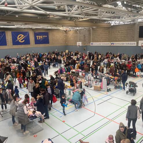 Volle Sporthalle mit vielen St&auml;nden auf einem Flohmarkt und zahlreichen Besuchern, die durch die G&auml;nge schlendern.