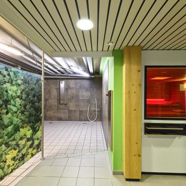 Eingang zu einem Wellnessbereich mit grünem Blattdesign und Blick auf eine Sauna mit rotem Licht hinter einer Glaswand.