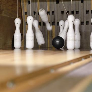 Schwarzer Bowlingball rollt auf eine Reihe weißer Kegel auf einer Holzbahn zu.
