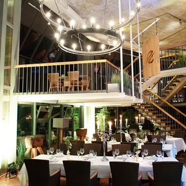 Moderne Restaurantinterior mit zwei Ebenen, eleganten Tischgedecken und einem großen Kronleuchter in stilvollem Ambiente.