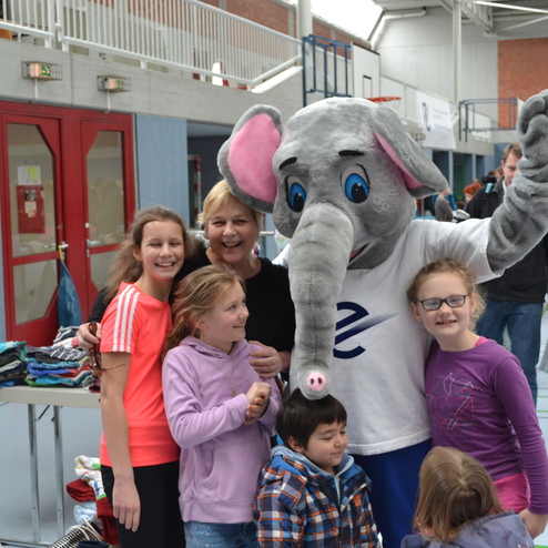 Gruppe von Kindern und einer Frau posieren mit einem verkleideten Elefanten in einer Sporthalle.