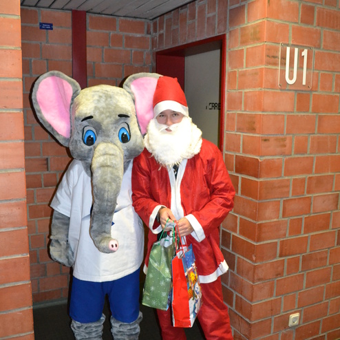 Ein Elefant in Kost&uuml;m und ein Mensch als Weihnachtsmann stehen in einem Flur vor einer T&uuml;r mit der Nummer U1.