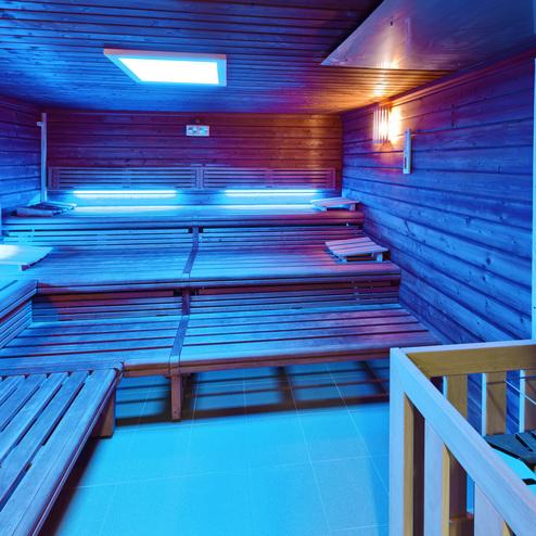 Innenansicht einer modernen Sauna mit blauen Lichtern und Holzliegen, ausgestattet mit einem Steinofen.