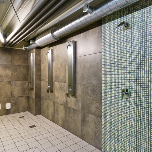Duschbereich mit drei Duschmöglichkeiten, gefliestem Boden und geblendetem Mosaik an der Wand.
