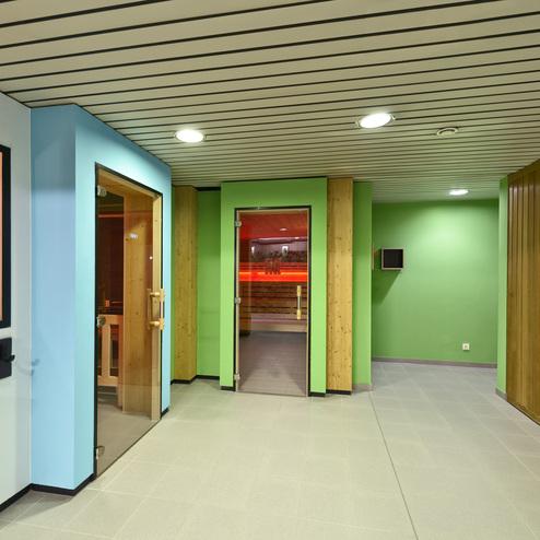 Modernes Saunainterieur mit grünen Wänden, Holzverkleidungen und mehreren Zugangstüren zu Saunen.