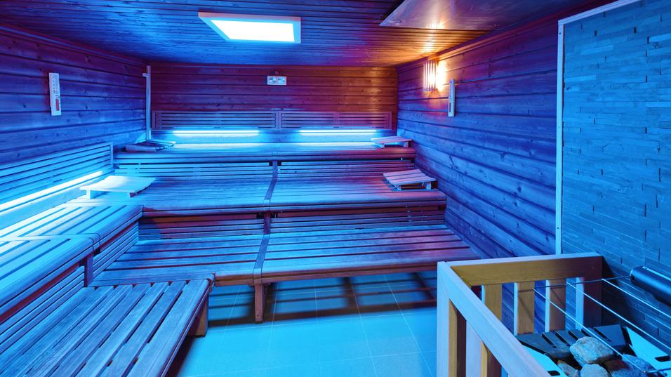 Innenansicht einer modernen Sauna mit blauen Lichtern und Holzliegen, ausgestattet mit einem Steinofen.