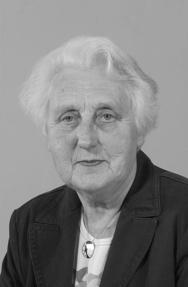 Portr&auml;t einer &auml;lteren Frau mit grauen Haaren und Brille, in einem schwarzen Blazer vor einem neutralen Hintergrund.