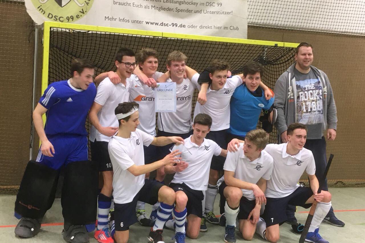 Gruppe junger Hockeyspieler posiert in Sportkleidung vor einem Hockeytor, lächelnd und feiernd nach einem Spiel.