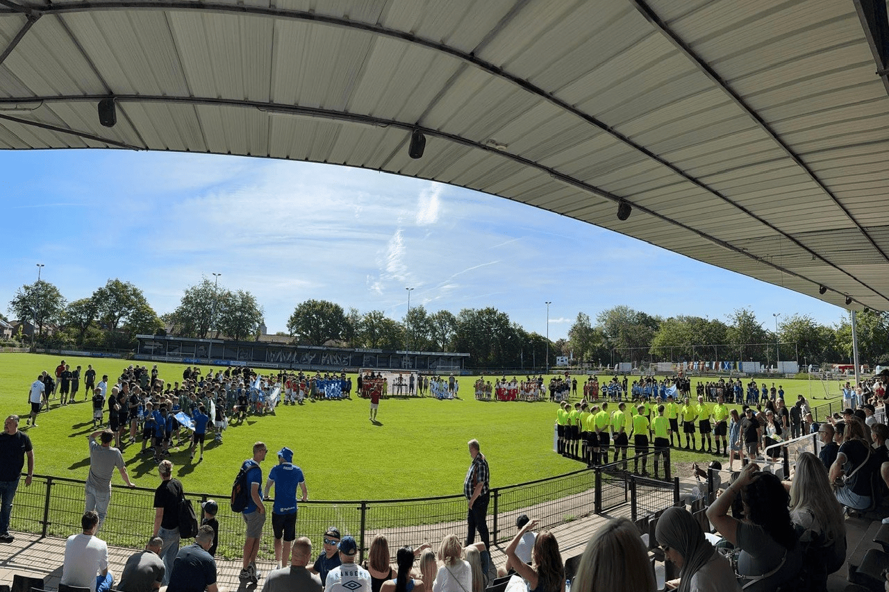 Gruppen von Fu&szlig;ballspielern und Schiedsrichtern stehen auf einem Rasenfeld, w&auml;hrend Zuschauer von den Trib&uuml;nen zuschauen.