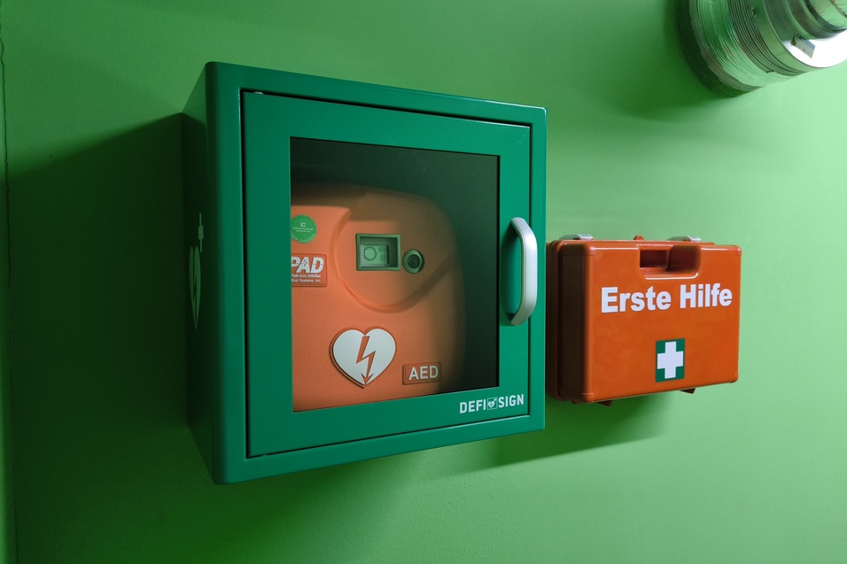 Defibrillator und Erste-Hilfe-Set in einem gr&uuml;nen Raum, montiert an der Wand.