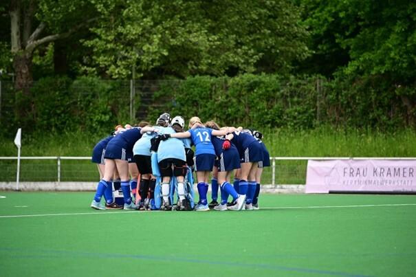 Mannschaft von Hockeyspielerinnen bildet einen Kreis auf dem Spielfeld zum gemeinsamen Anfeuern vor dem Spiel.