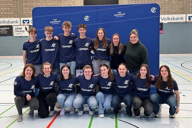 Gruppe junger Menschen in blauen T-Shirts posiert l&auml;chelnd vor einer Wand mit dem Logo des TSC Eintracht.