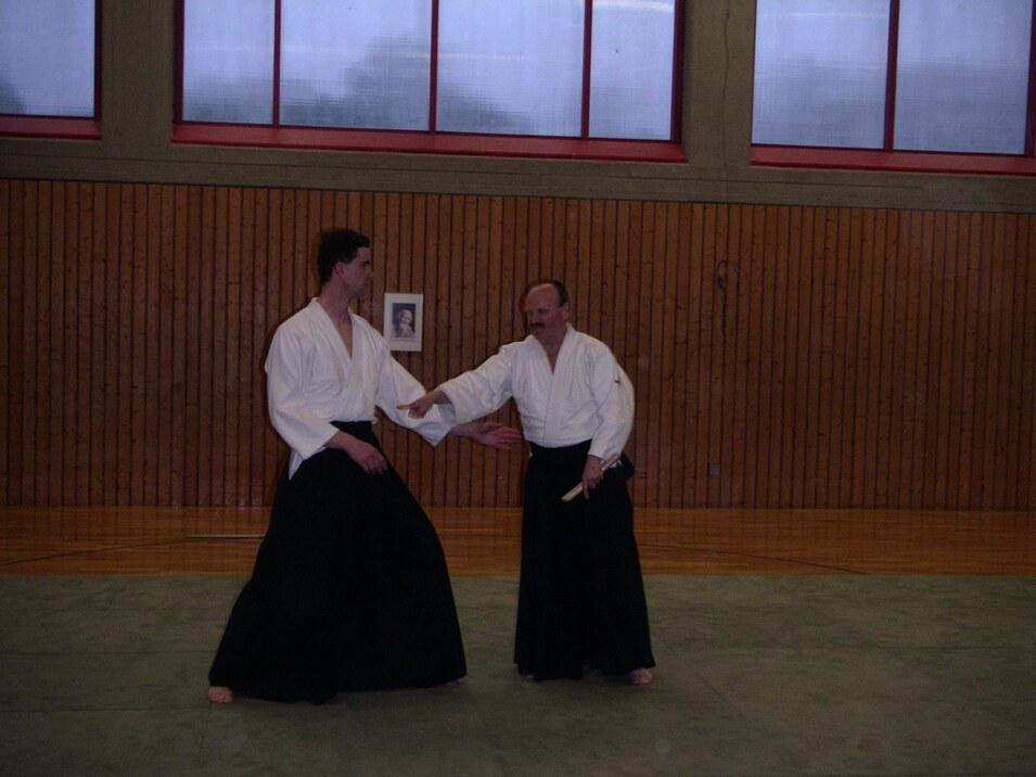 Zwei Aikido-Praktizierende in traditionellen Gewändern üben eine Technik auf einer Tatami-Fläche.