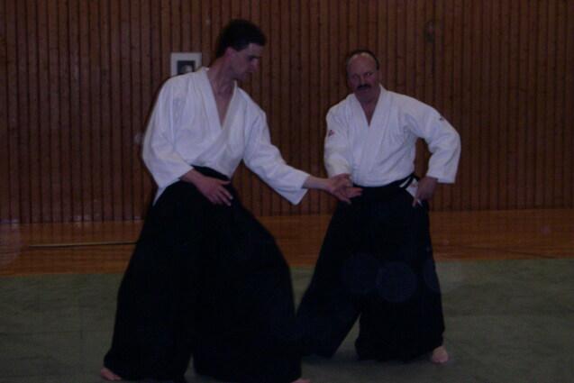 Zwei Männer in traditioneller Bujutsu-Kleidung zeigen eine Technik auf einer Tatami-Matte in einem Trainingsraum.