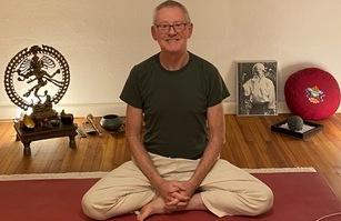 Mann im Schneidersitz auf einer Yogamatte, umgeben von Meditationsutensilien und dekorativen Elementen.