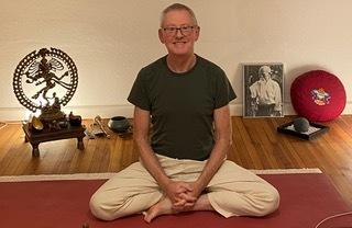 Mann im Schneidersitz auf einer Yogamatte, umgeben von Meditationsutensilien und dekorativen Elementen.