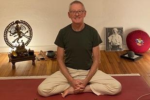 Mann im Schneidersitz auf einer Yogamatte, umgeben von Meditationsutensilien und dekorativen Elementen.