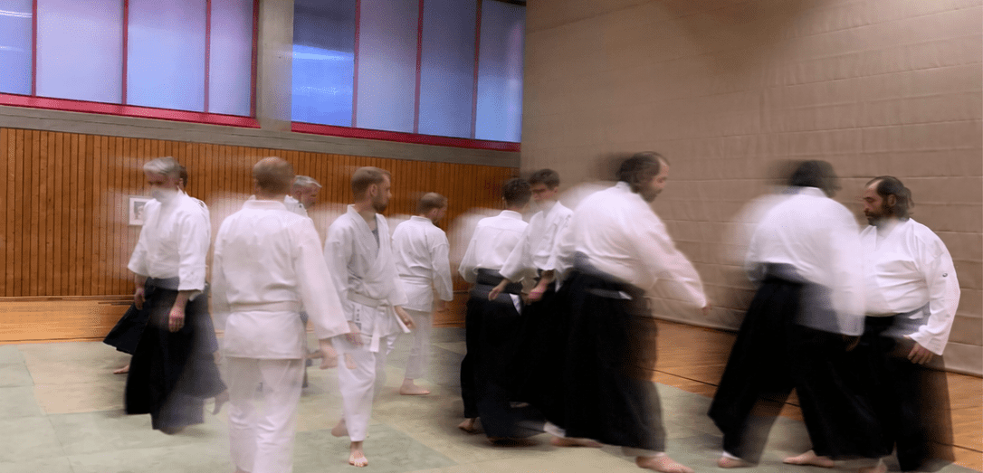 Gruppe von Aikido-Praktizierenden in wei&szlig;en und schwarzen Anz&uuml;gen trainiert in einem Sportraum.